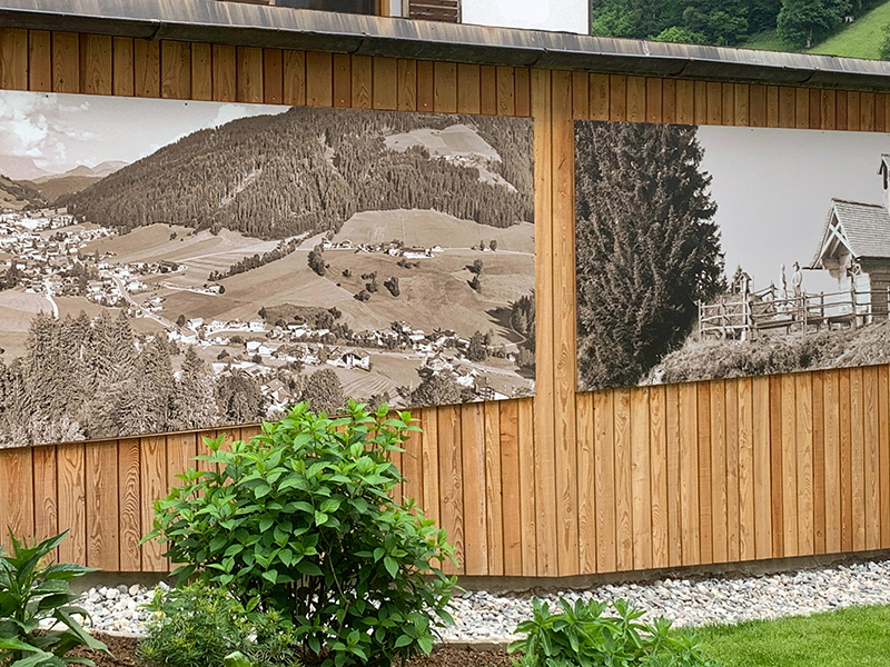 Großformatige Wandbilder mit historischen Landschaftsmotiven auf einer Holzfassade